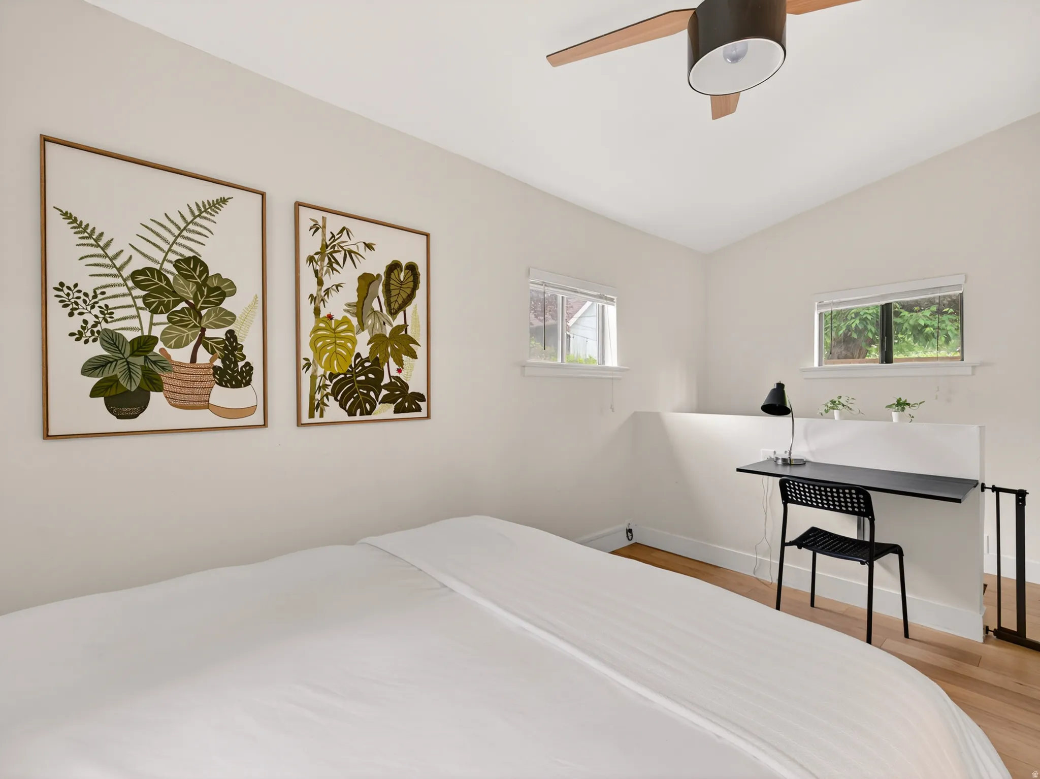 Bright room featuring wood-finish flooring, two large windows, a built-in desk, and a ceiling fan with light fixture