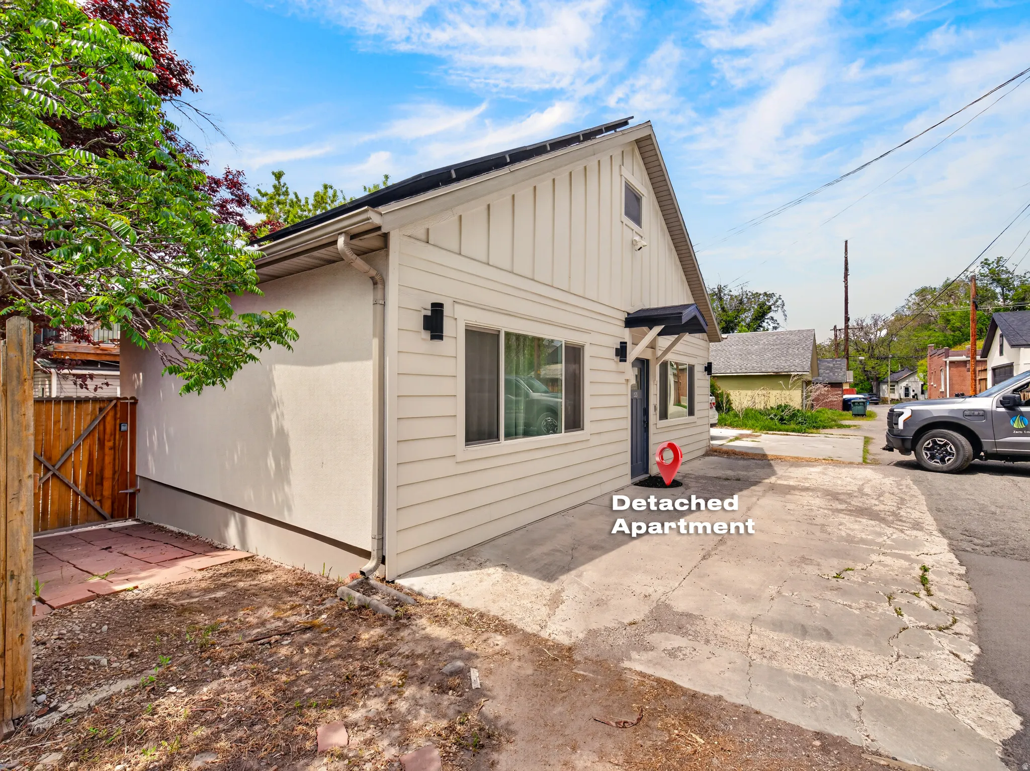 Detached apartment featuring light-toned horizontal siding with vertical siding accents, dark entry door with a small awning, and an exterior wall sconce