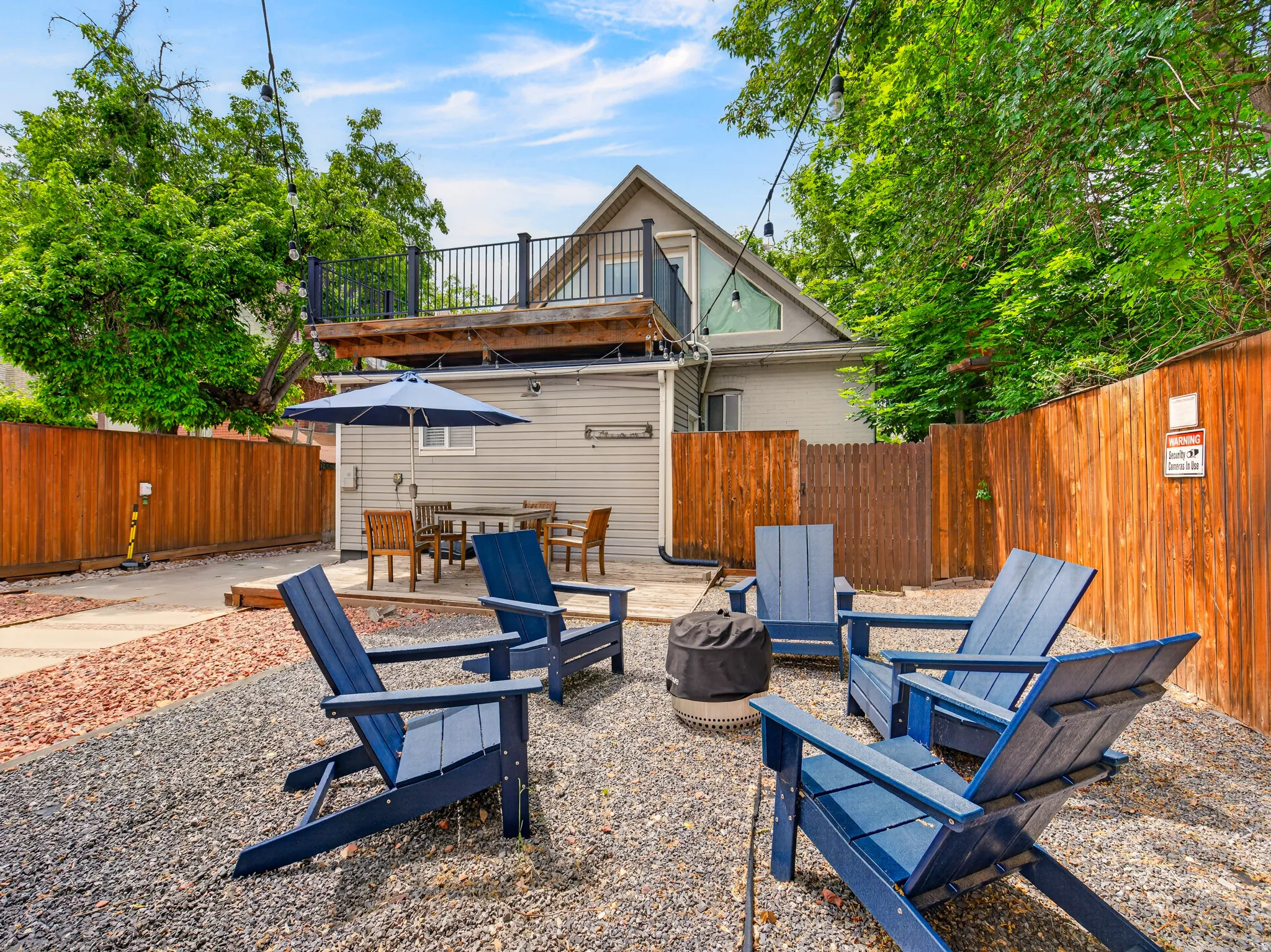 Backyard featuring a gravel patio area with a fire pit, a wooden privacy fence, a second-story balcony with metal railings, a paved pathway, and exterior siding