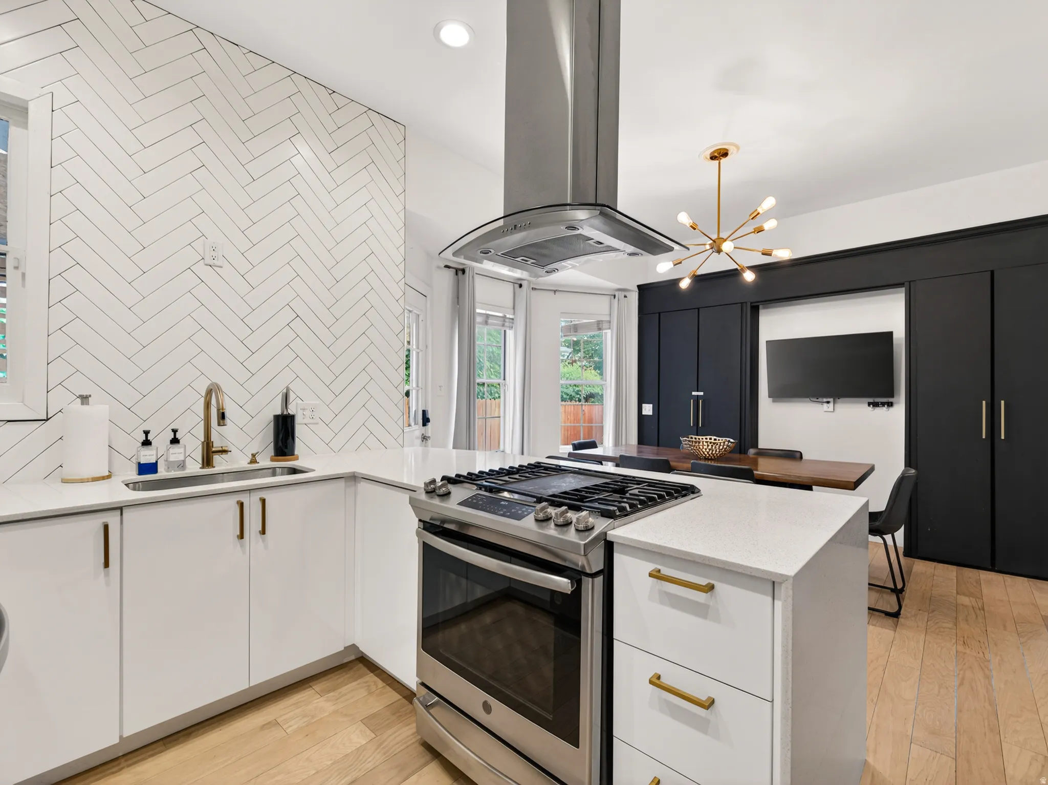 Modern kitchen featuring white cabinetry, quartz countertops, a herringbone tile backsplash, and stainless steel appliances including a range with a hood