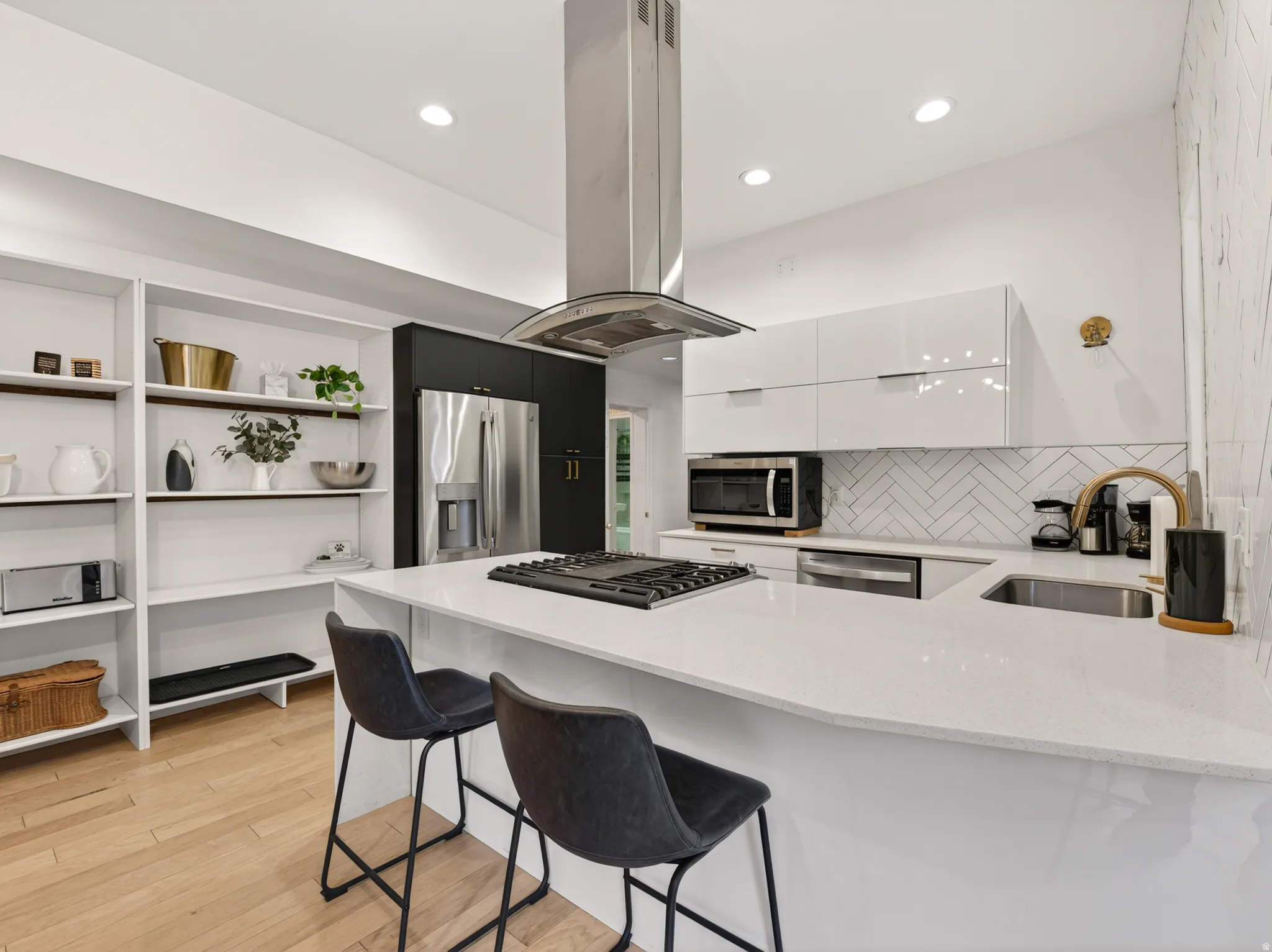 Gourmet kitchen featuring a built-in stainless steel refrigerator, white gloss cabinetry, a herringbone tile backsplash, a stainless steel range hood, and a large central island with a sink and cooktop