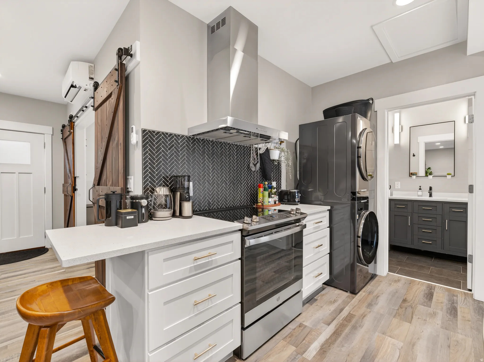 Kitchen featuring a herringbone tile backsplash, stainless steel range with overhead hood, white cabinetry with gold-tone hardware, and a white countertop