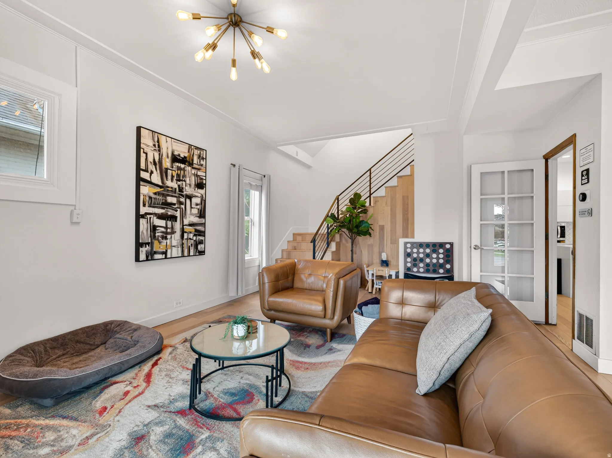 Light-filled living area featuring wood-finish flooring, a modern sputnik chandelier, and a prominent staircase with contemporary metal railings
