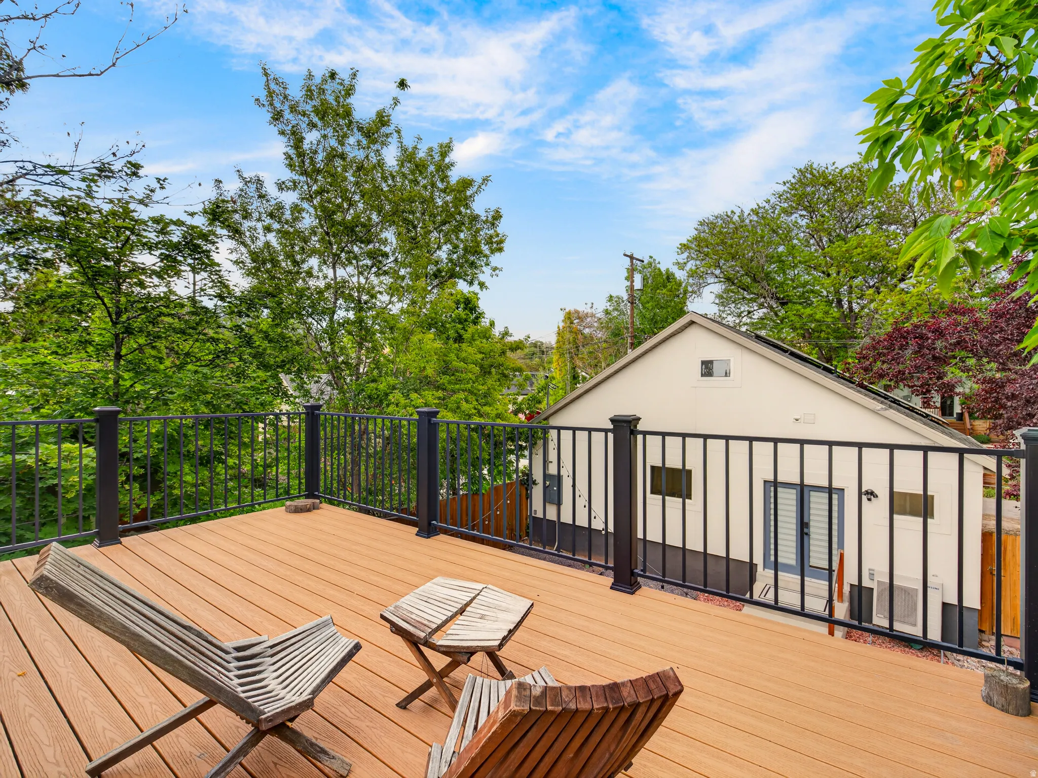 Spacious outdoor deck featuring composite decking, black metal railings, and ample tree coverage