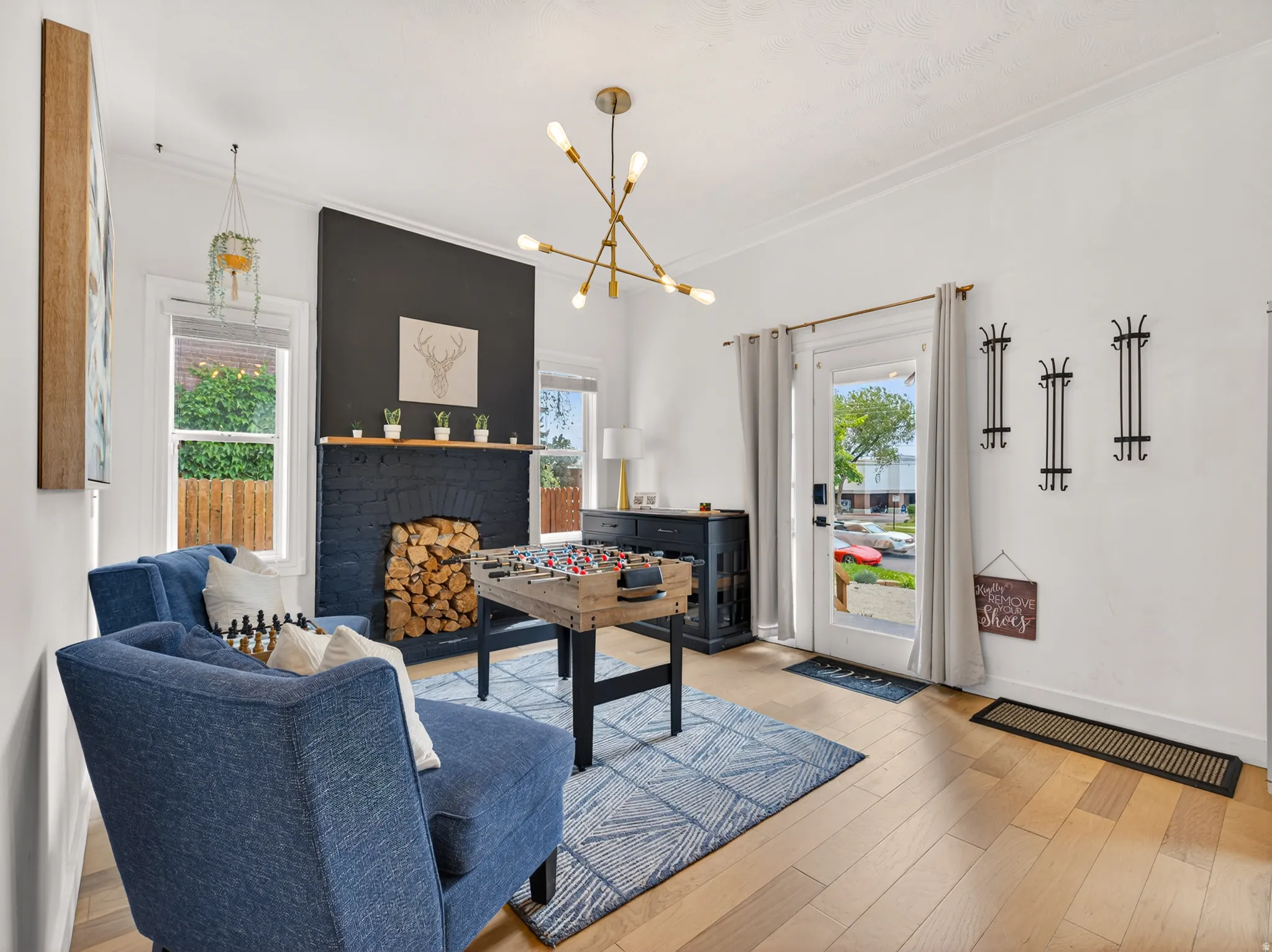 Living area featuring wood-finish flooring, a painted brick fireplace with a wood mantle, an accent wall, and a gold-finish chandelier
