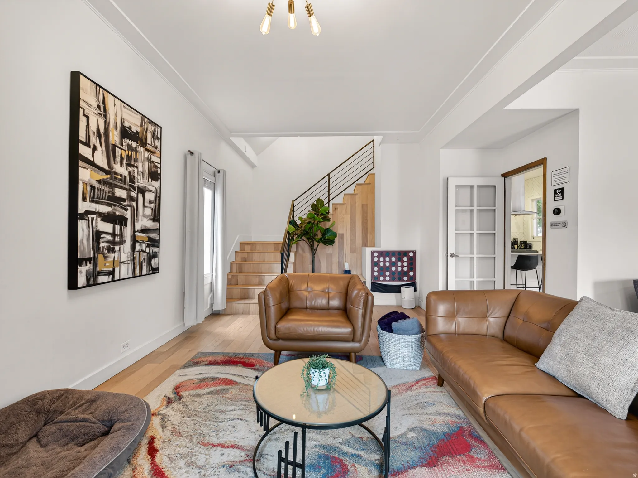 Bright living space featuring light wood-finish flooring, a modern open-tread staircase with metal railing, and a multi-pane glass door