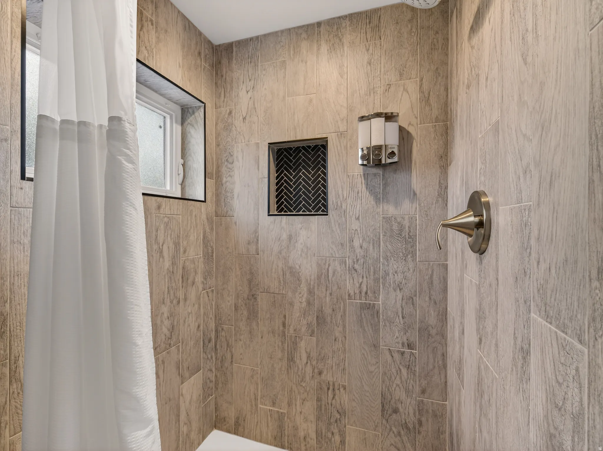 Shower enclosure featuring wood-finish tile, a built-in niche with herringbone tile, an integrated window, a brushed nickel shower fixture, and a white shower base