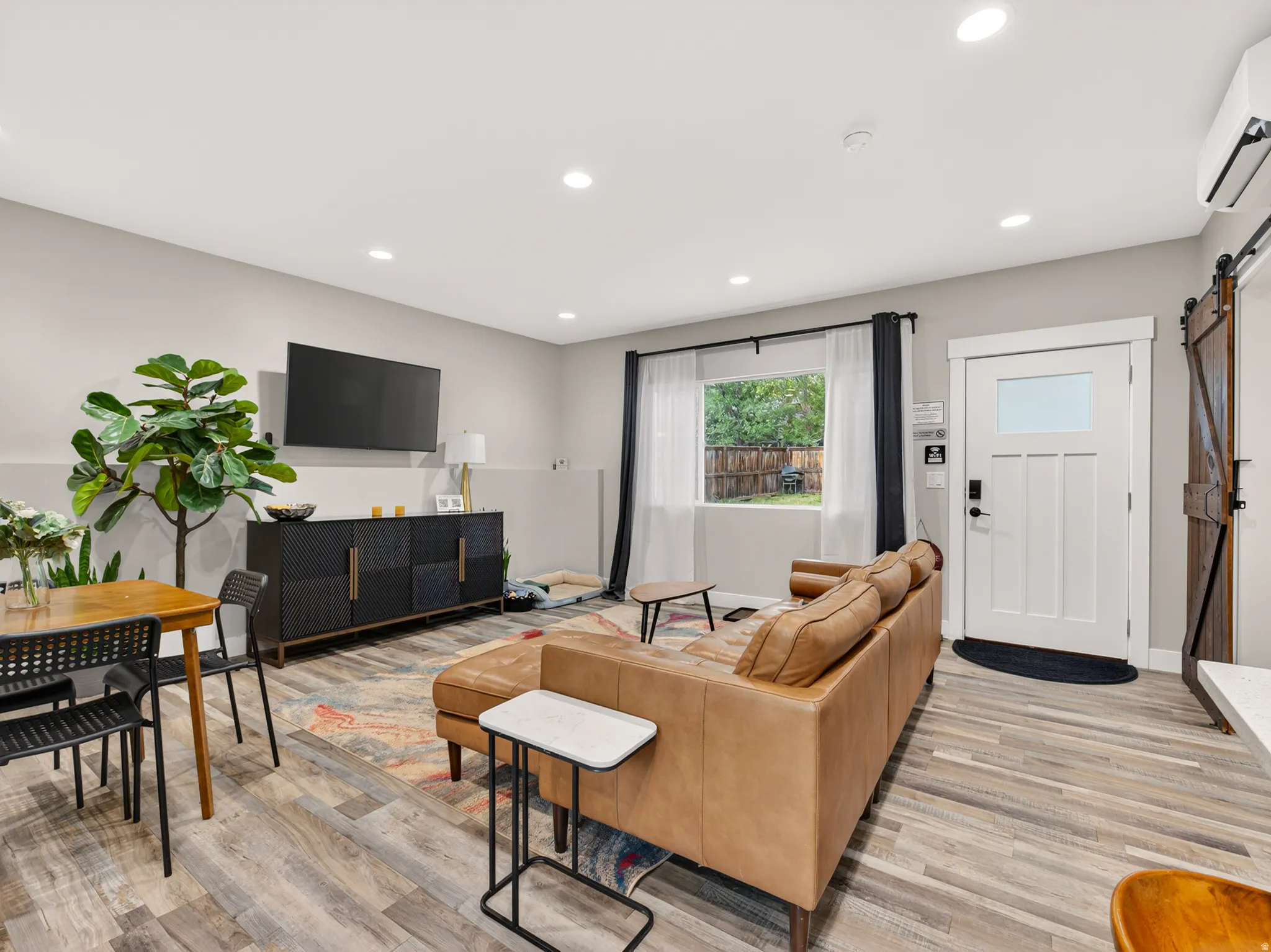Open-concept living area featuring wood-finish flooring, recessed lighting, and a white craftsman-style entry door with frosted glass