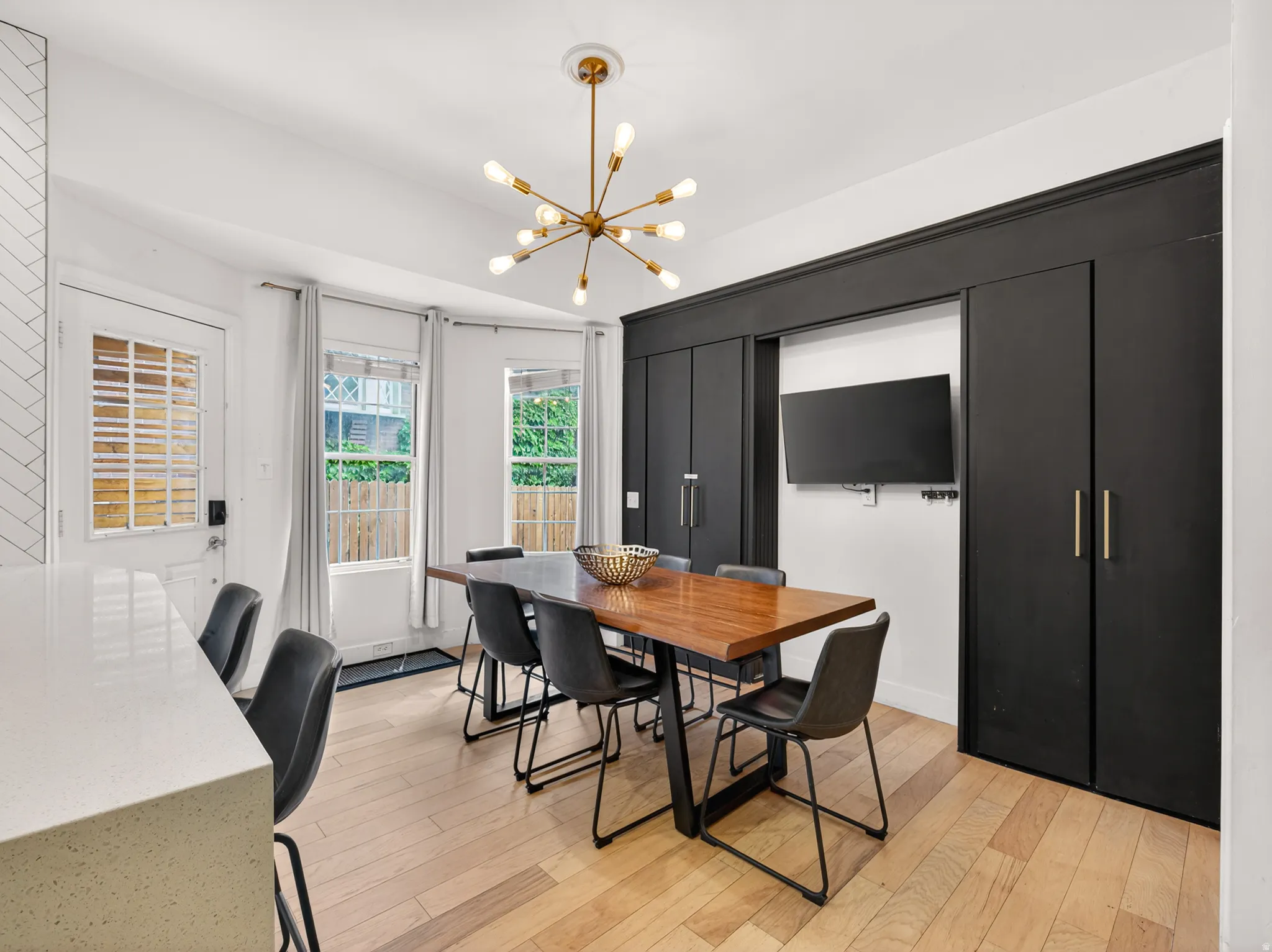 Dining area featuring wood-finish flooring, a modern sputnik chandelier, built-in cabinetry with gold-tone hardware, and a white countertop breakfast bar