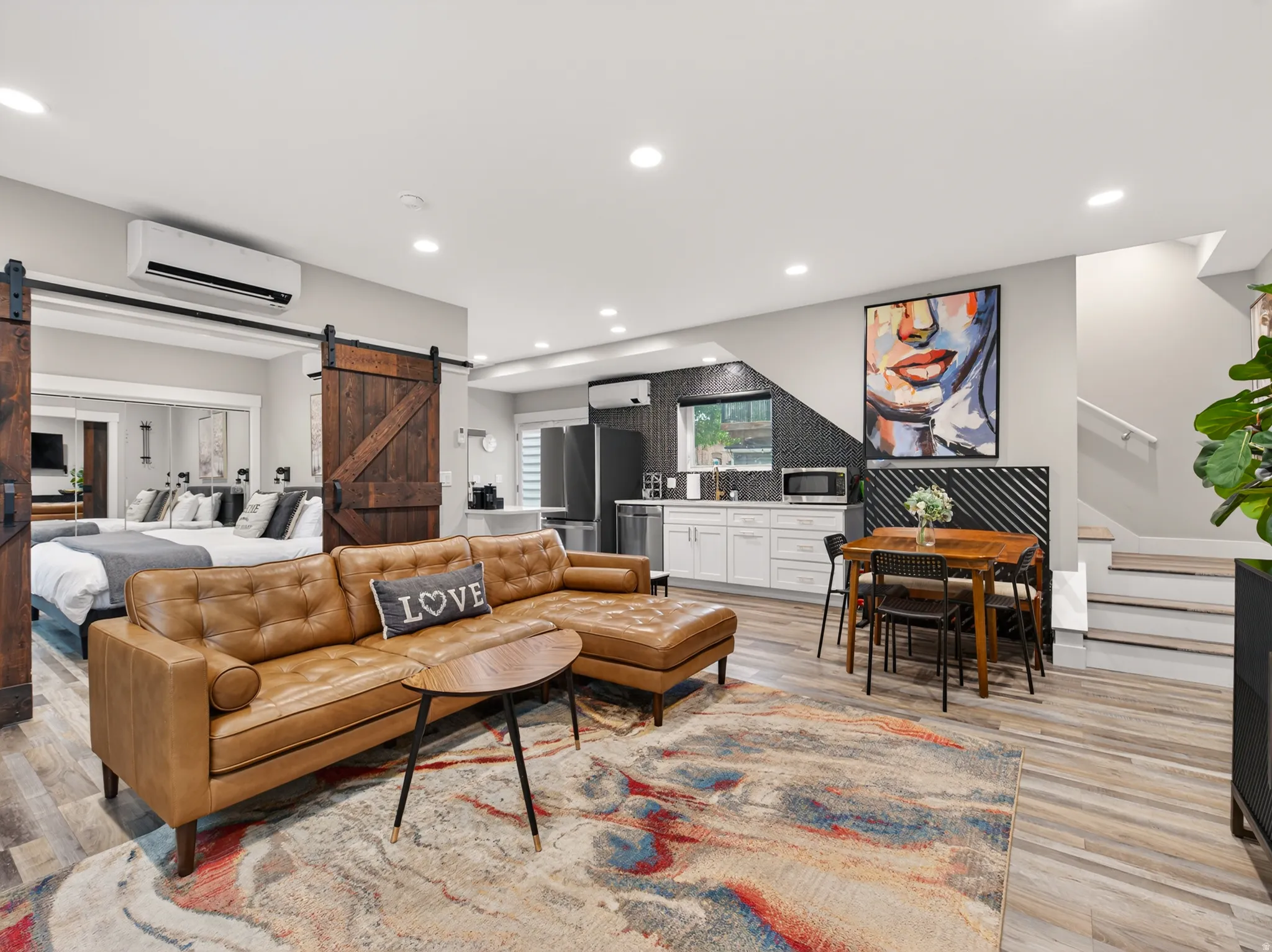 Open-concept living space featuring wood-finish flooring, recessed lighting, and a kitchen area with white cabinetry and black tile backsplash