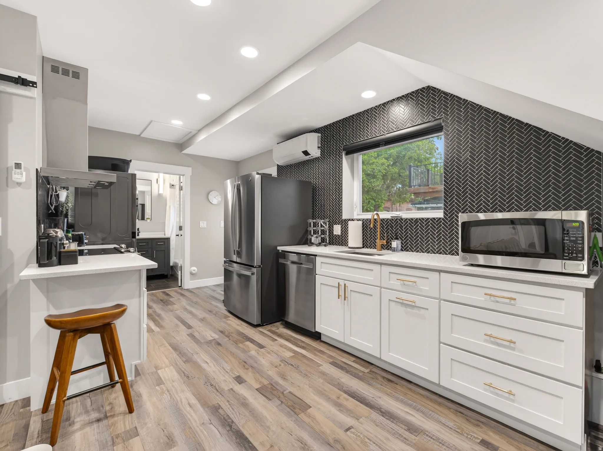 Kitchen featuring wood-finish flooring, white cabinetry with gold-tone hardware, a herringbone pattern accent wall, stainless steel appliances, and recessed lighting