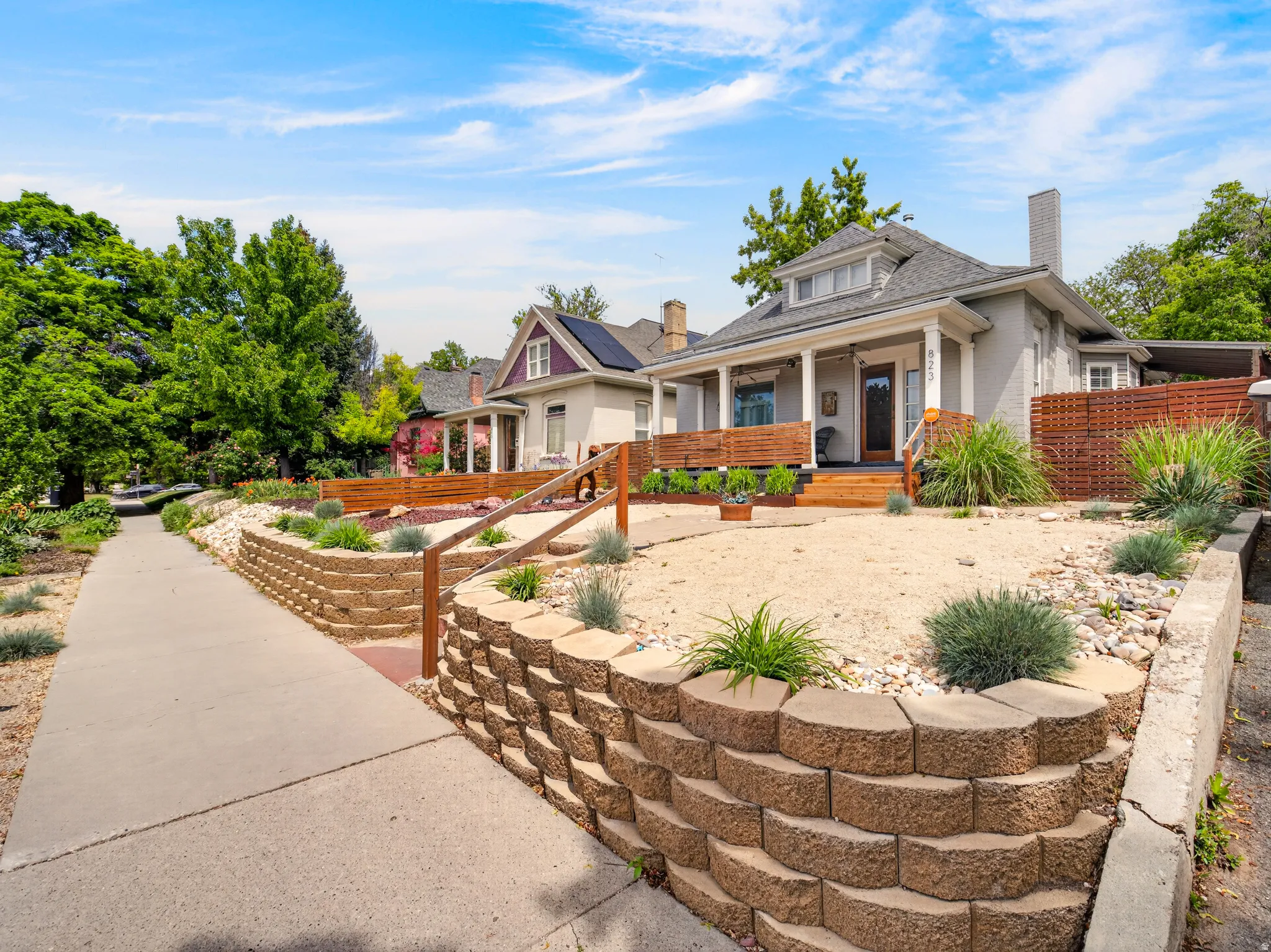 Elevated residence featuring a covered porch with white columns, a wood-finish fence, and a stone retaining wall