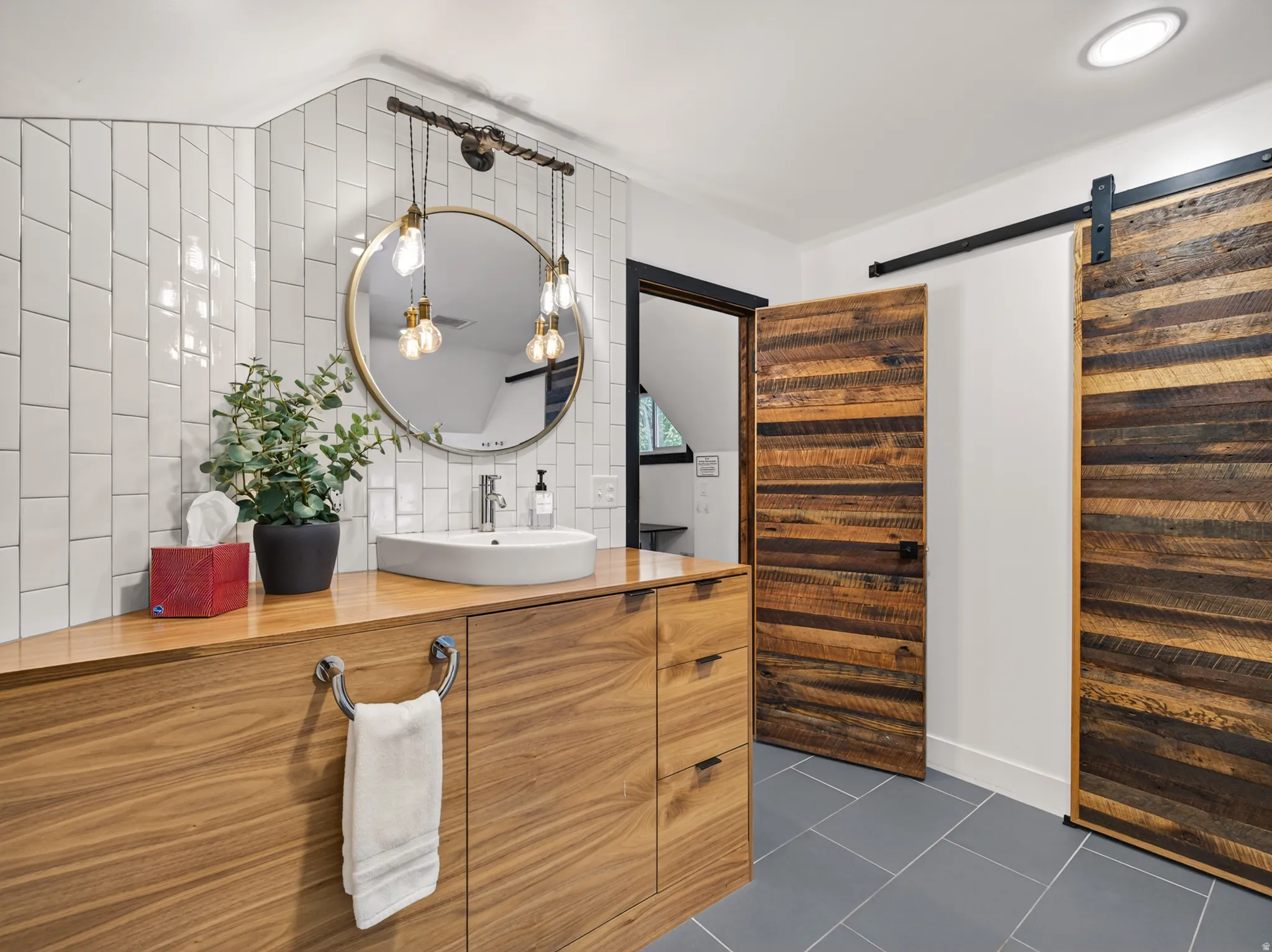 Bathroom featuring a wood-finish vanity with a vessel sink, a round mirror, and a three-bulb vanity light fixture
