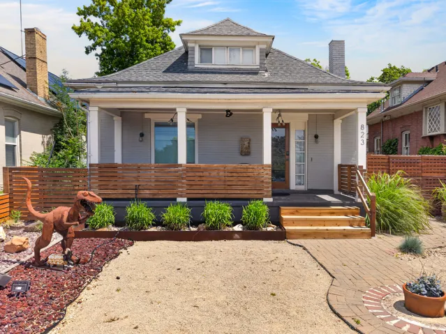 Gable-front bungalow featuring a covered porch with white columns, wood privacy screening, and a brick paver pathway