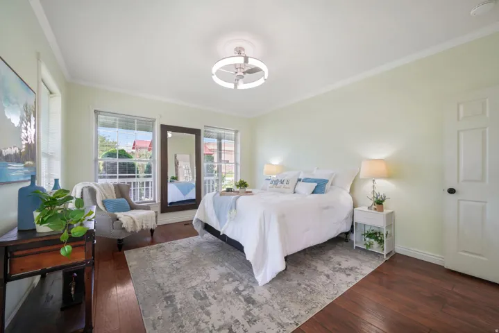 Spacious bedroom featuring rich wood-finish flooring, light-toned walls, and crown molding