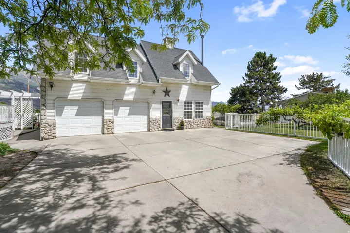 White siding exterior with a dark shingle roof, stone accents, two garage doors, and a concrete driveway