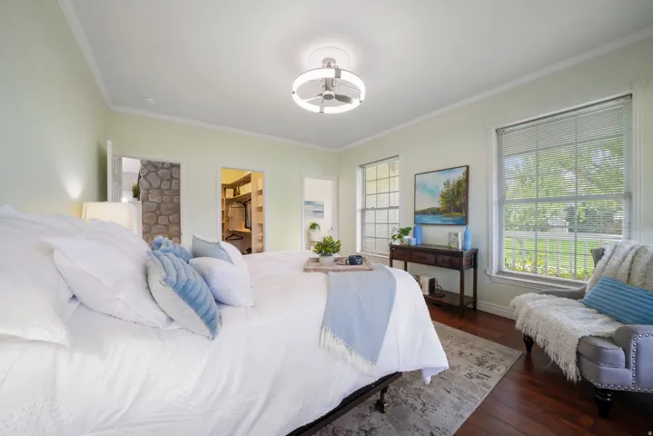 Spacious bedroom featuring wood-finish flooring, light-toned walls with crown molding, and a modern ceiling fan fixture