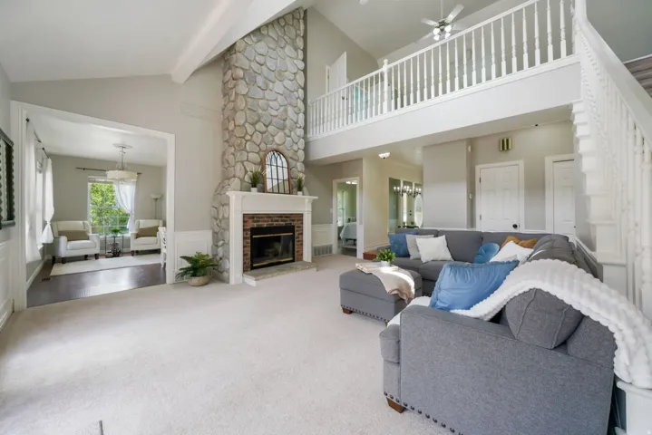 Two-story living area featuring a stone and brick fireplace with a white mantel, vaulted ceilings, and a second-story balustrade