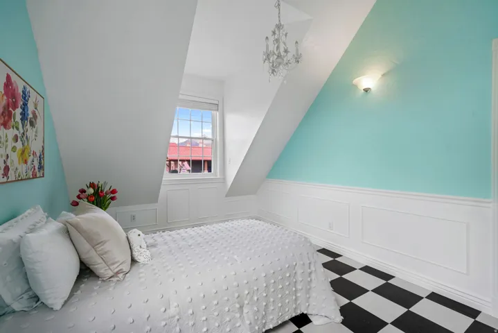 Attic space featuring a window, sloped ceilings, beadboard wainscoting, checkered flooring, and a chandelier