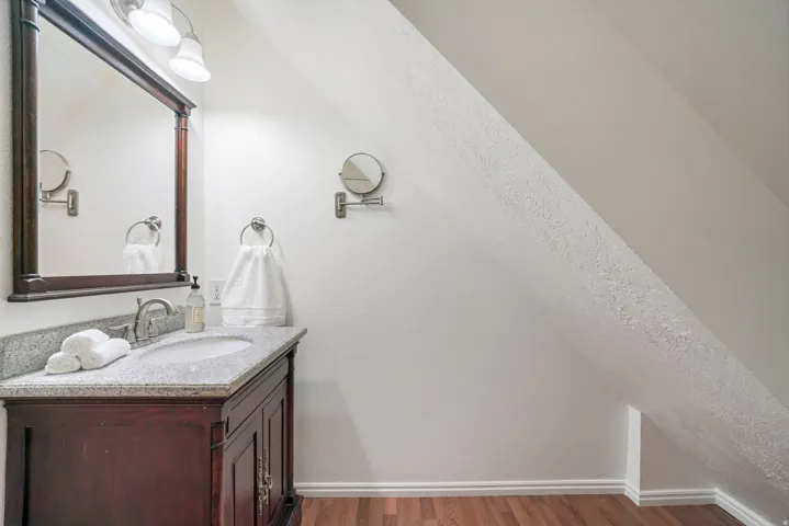 Vanity featuring a granite-finish countertop with an undermount sink, wood-finish cabinetry, and a framed mirror