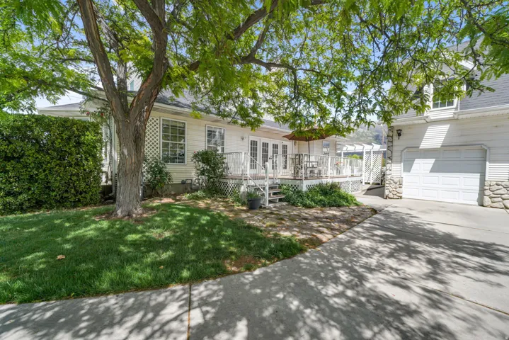 Exterior featuring a white siding finish, a multi-level deck with white railings, a concrete driveway, a two-car garage with stone accents, and a mature tree providing natural shade