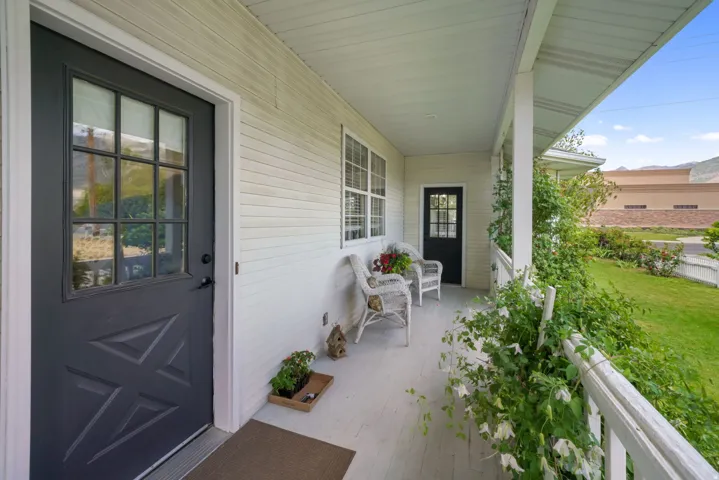 Covered front porch featuring a dark entry door with glass paneling, white horizontal siding, and a white railing with greenery