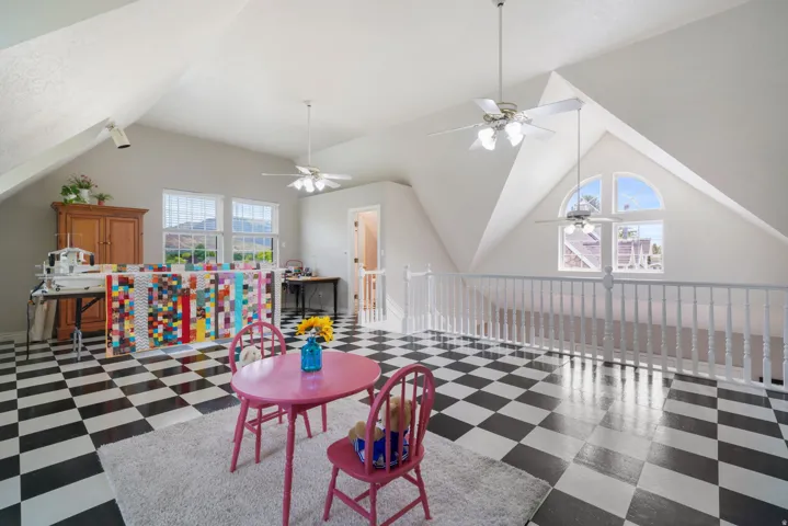 Spacious loft area featuring vaulted ceilings, black and white checkerboard flooring, multiple windows providing natural light, a half-round architectural window, and three ceiling fans