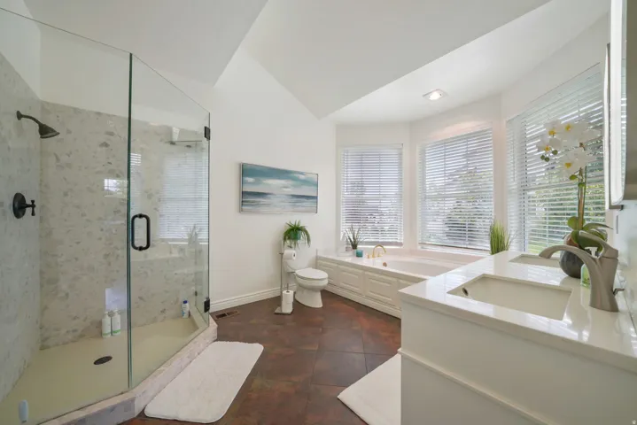 Bathroom featuring a glass-enclosed shower with stone-finish tile, a built-in soaking tub, dual vanity with undermount sinks and quartz countertops, and rich-toned floor tiles