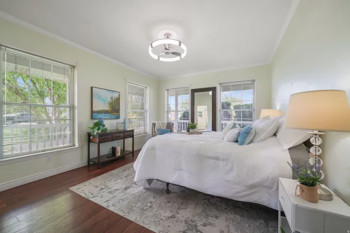 Spacious room featuring rich wood-finish flooring, multiple windows with blinds, crown molding, and a contemporary ceiling fixture