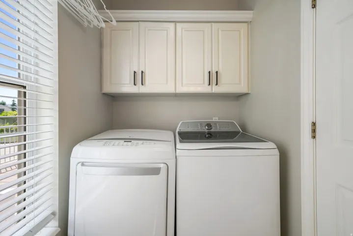 Dedicated laundry area featuring upper cabinetry with dark hardware, a white door, and a window with blinds
