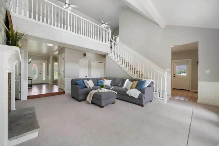 Spacious living area featuring a vaulted ceiling with exposed beams, an open mezzanine, and a grand staircase with white balusters