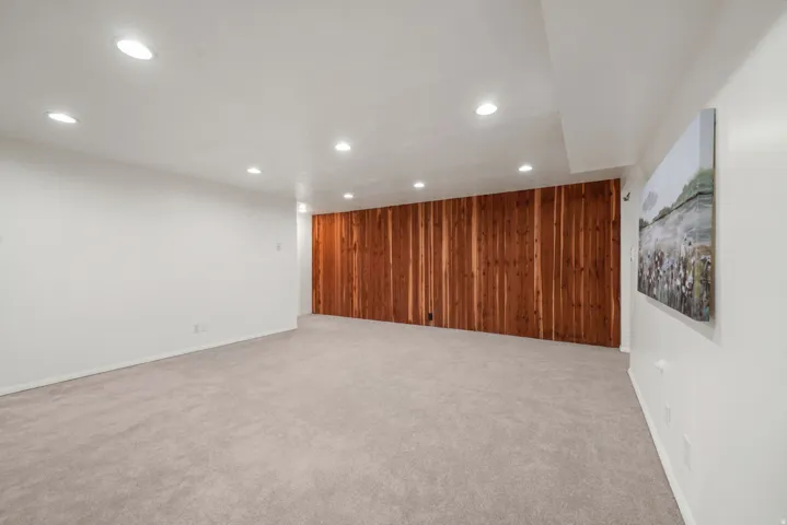 Spacious room featuring a prominent wood plank accent wall, recessed lighting, light-toned carpeting, and crisp white walls