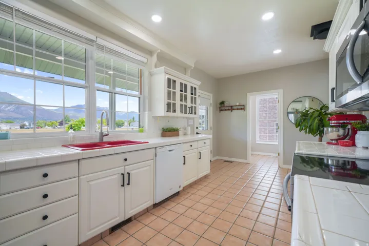 Kitchen featuring multiple windows with mountain scenery, white cabinetry, tile countertops, tile backsplash, and tile flooring