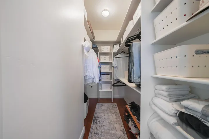 Walk-in closet featuring extensive built-in shelving, hanging rods, and wood-finish flooring