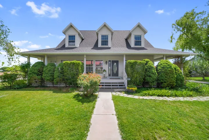 Cottage-style home featuring a full-width covered front porch, dormer windows, a symmetrical facade, and a paved walkway leading to the entrance