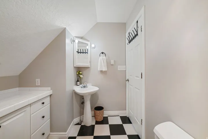 Pedestal sink with wall-mounted lighting, medicine cabinet, and black and white checkered flooring