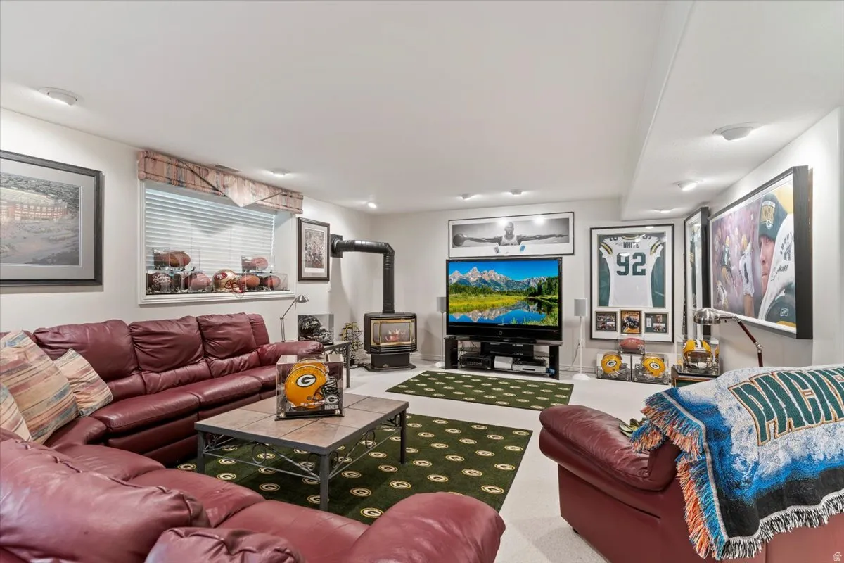 Spacious lower-level room featuring a wood-burning stove with a visible flue, recessed ceiling lighting, and a window with horizontal blinds