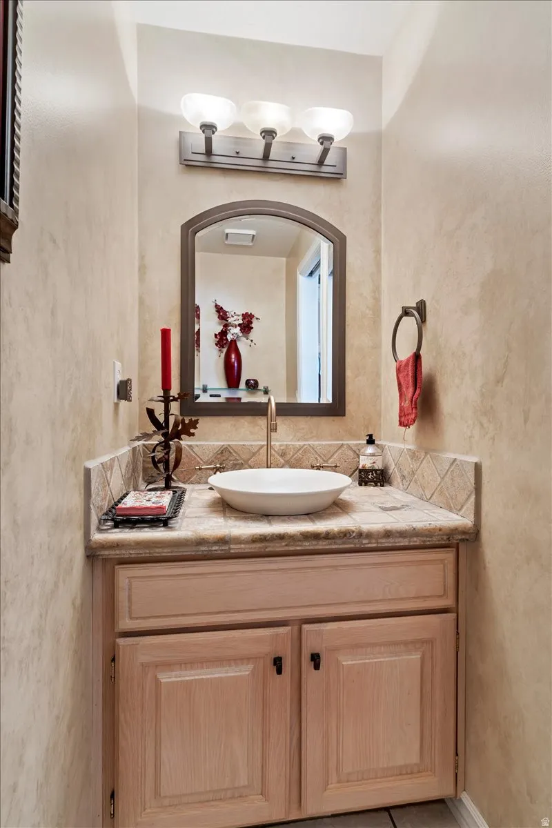 Vanity featuring a vessel sink, tile countertop, and tile backsplash