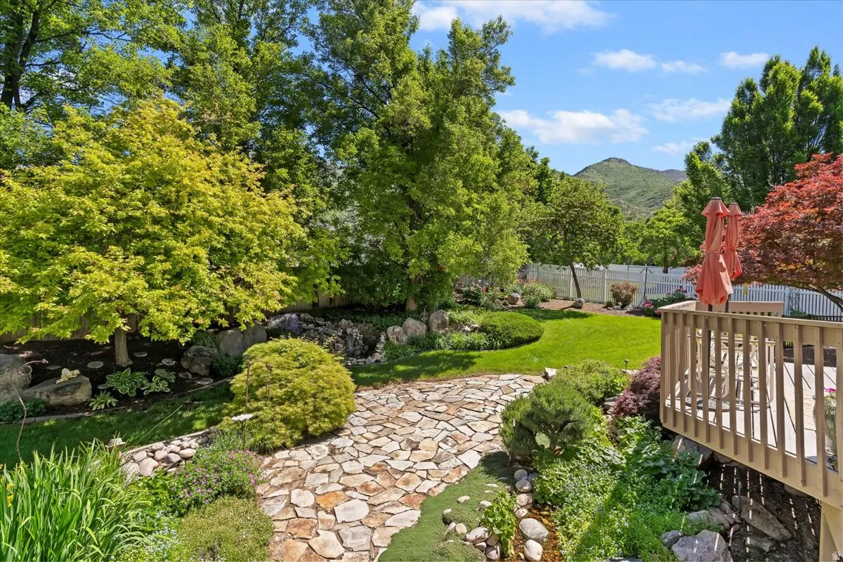 Expansive backyard featuring a stone pathway, varied mature trees, a manicured lawn, and a multi-level wooden deck