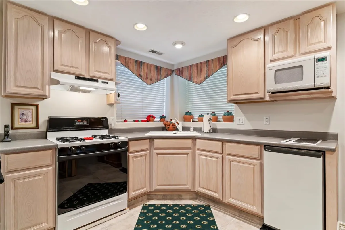 Corner kitchen featuring light wood-finish cabinetry, a gas range with an overhead vent, and a built-in microwave