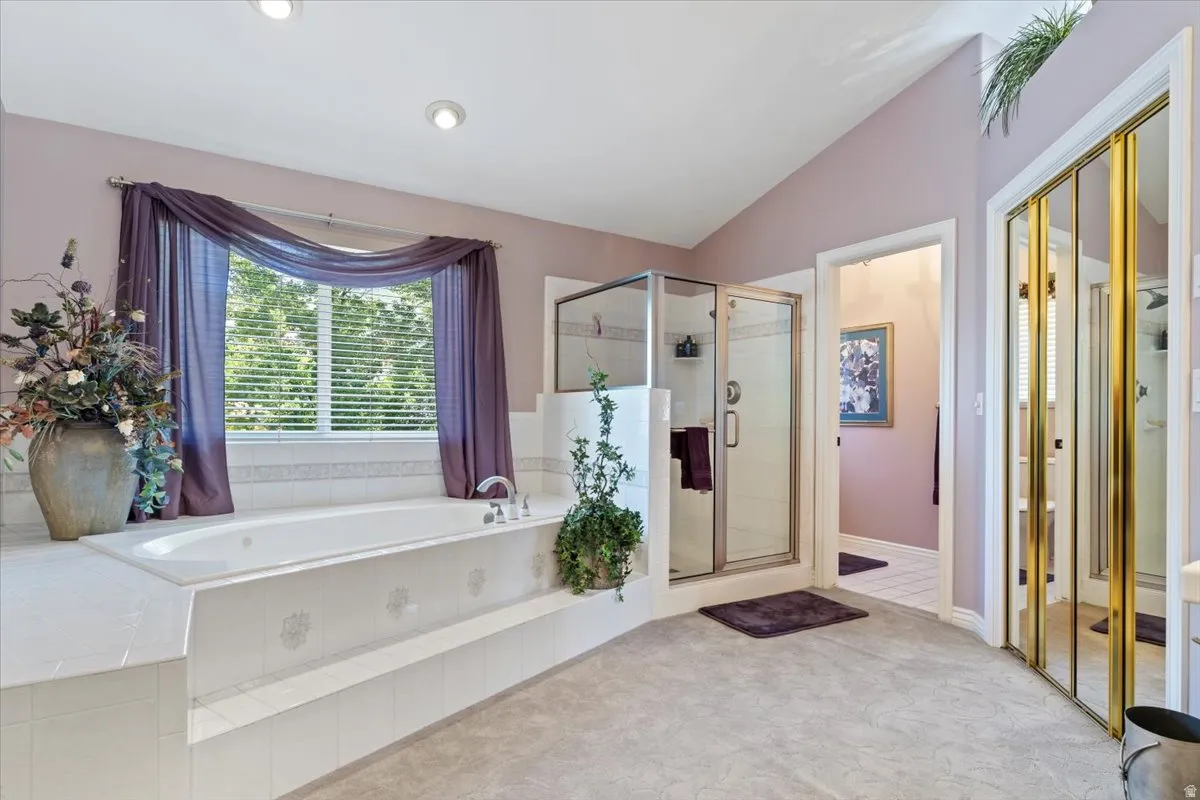 Soaking tub with tiled surround, glass-enclosed shower, vaulted ceiling, recessed lighting, and mirrored closet doors