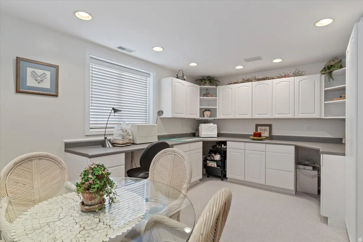 Bright room featuring extensive white cabinetry with upper and lower storage, a built-in desk area, recessed lighting, and a window with horizontal blinds