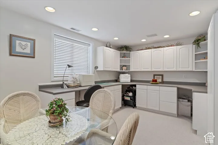 Bright room featuring extensive white cabinetry with upper and lower storage, a built-in desk area, recessed lighting, and a window with horizontal blinds