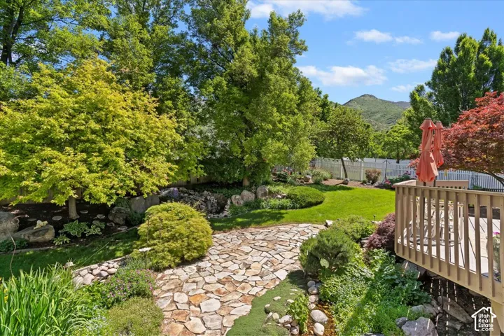 Expansive backyard featuring a stone pathway, varied mature trees, a manicured lawn, and a multi-level wooden deck