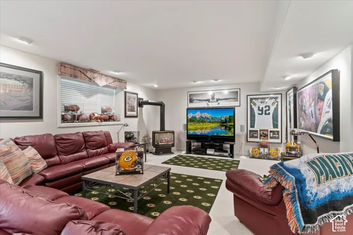 Spacious lower-level room featuring a wood-burning stove with a visible flue, recessed ceiling lighting, and a window with horizontal blinds