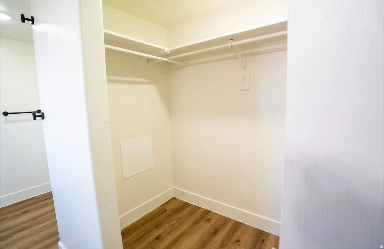 Corner closet featuring wood-finish flooring, white walls, built-in shelving, and hanging rods