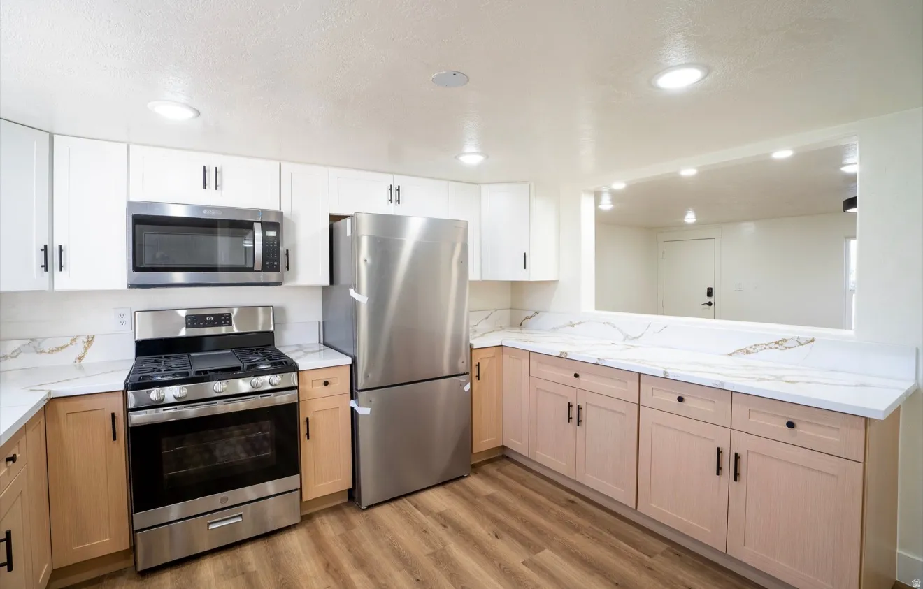 Contemporary kitchen featuring stainless steel appliances, two-tone cabinetry, wood-finish flooring, recessed lighting, and a pass-through window