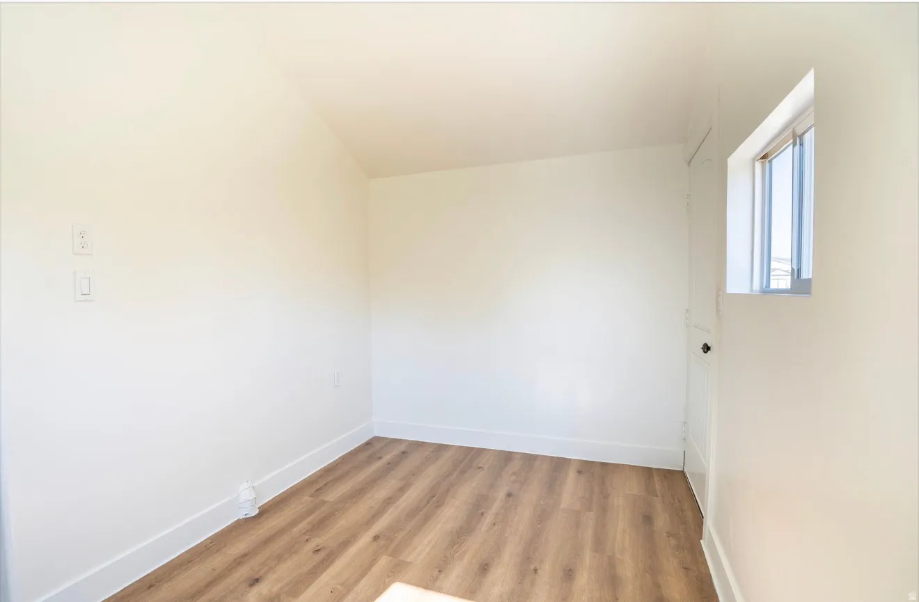 Interior room featuring wood-finish flooring, white baseboards, a single window, and a white door with a black knob