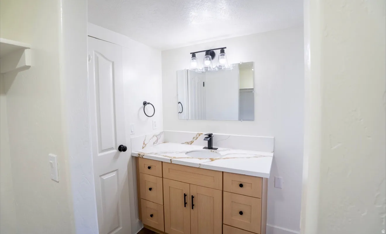 Bathroom vanity featuring a light wood-finish cabinet with black hardware, a white countertop with subtle veining, an undermount sink, and a matte black faucet