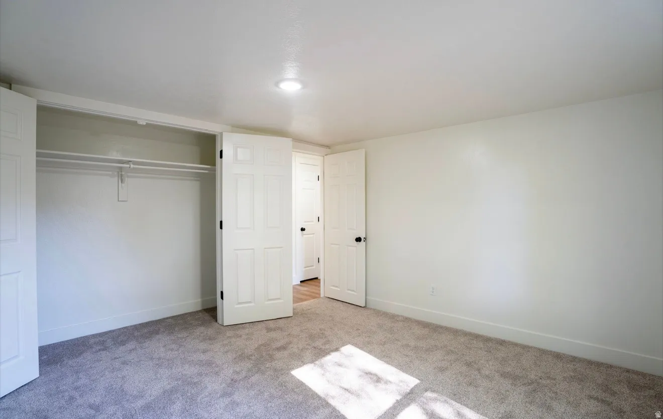 Bedroom featuring gray carpeting, white walls, white baseboards, a flush-mount ceiling light, and a double-door closet with shelving and hanging rods